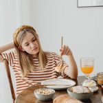 Teen girl in striped shirt at breakfast table with fruits, bread, and juice. Casual morning setting.